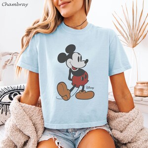 以下が含まれることがあります： ミッキーマウスのグラフィックが特徴のライトブルーのTシャツ。漫画のキャラクターは、象徴的な赤いショートパンツ、茶色の靴、黒い耳で描かれています。ディズニーのロゴが見えます。柔らかい素材で作られたシャツです。