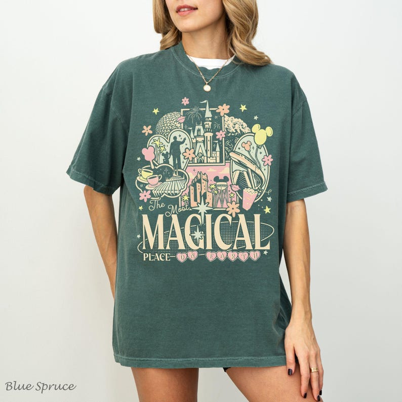 May include: A dark green short-sleeve t-shirt featuring a graphic print with a castle, stars, flowers, and the text "The Most MAGICAL PLACE ON EARTH". The design includes light yellow, pink, and white colors, with a crew neckline and loose fit.
