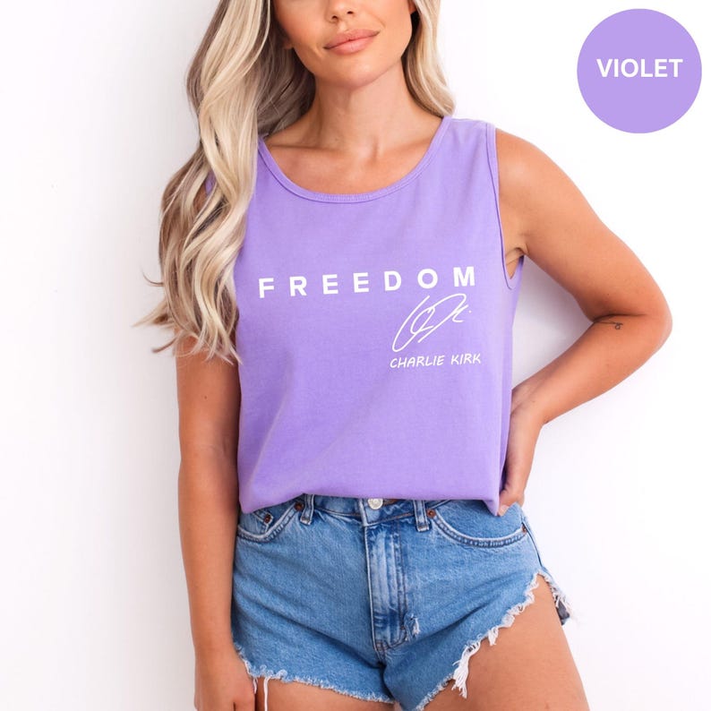 Puede incluir: Una camiseta sin mangas violeta con la palabra "FREEDOM" impresa en blanco, junto con una firma y el nombre "CHARLIE KIRK". La camiseta sin mangas se combina con pantalones cortos de mezclilla. Un c&iacute;rculo violeta con la palabra "VIOLET" est&aacute; en la esquina superior derecha.