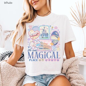 May include: White t-shirt with a colorful graphic design featuring various theme park attractions. The design includes a monorail, a castle, and the text "The most MAGICAL PLACE ON EARTH."