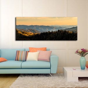 Puede incluir: Una fotograf&iacute;a panor&aacute;mica de una cordillera con una puesta de sol dorada en el fondo. Las monta&ntilde;as est&aacute;n cubiertas de &aacute;rboles y el cielo es de un azul suave con algunas nubes. La imagen est&aacute; tomada desde un punto de vista elevado, mirando hacia el paisaje.