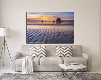 May include: A rectangular wall art print featuring a sunset landscape of a beach with rippled sand, distant rock formations, and a vibrant orange and blue sky. The print is displayed on a wall above a light gray sofa with chevron pillows.