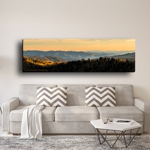 Puede incluir: Una fotograf&iacute;a panor&aacute;mica de una cordillera con una puesta de sol dorada en el fondo. Las monta&ntilde;as est&aacute;n cubiertas de &aacute;rboles y el cielo es de un azul suave.