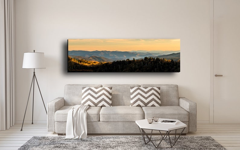 Puede incluir: Una fotograf&iacute;a panor&aacute;mica de una cordillera con una puesta de sol dorada en el fondo. Las monta&ntilde;as est&aacute;n cubiertas de &aacute;rboles y el cielo es de un azul suave.
