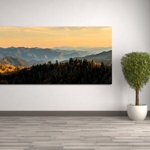 Puede incluir: Una fotograf&iacute;a panor&aacute;mica de una cordillera con una puesta de sol dorada en el fondo. Las monta&ntilde;as est&aacute;n cubiertas de &aacute;rboles y el cielo es de un azul suave. La imagen est&aacute; tomada desde un punto de vista elevado, mirando hacia abajo a las monta&ntilde;as.