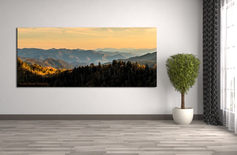 Puede incluir: Una fotograf&iacute;a panor&aacute;mica de una cordillera con una puesta de sol dorada en el fondo. Las monta&ntilde;as est&aacute;n cubiertas de &aacute;rboles y el cielo es de un azul suave. La imagen est&aacute; tomada desde un punto de vista elevado, mirando hacia abajo a las monta&ntilde;as.