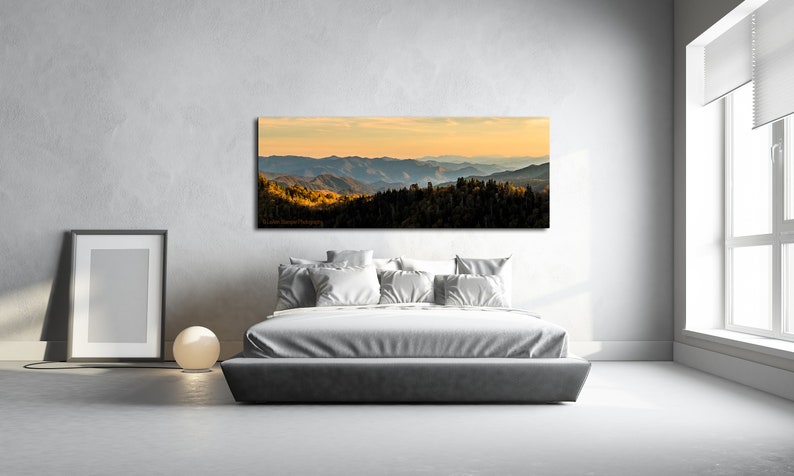 Puede incluir: Una fotograf&iacute;a panor&aacute;mica de una cordillera con una puesta de sol dorada en el fondo. Las monta&ntilde;as est&aacute;n cubiertas de &aacute;rboles y el cielo es de un azul suave. La imagen est&aacute; enmarcada y colgada en una pared sobre una cama en un dormitorio.
