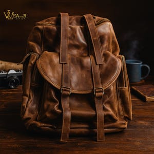 May include: A brown leather backpack with adjustable straps and multiple pockets. The bag features a flap closure with buckles and a zippered main compartment. The leather has a distressed look, giving it a vintage aesthetic. The backpack is designed for carrying items.