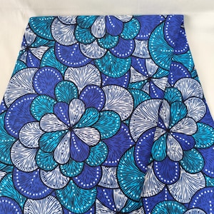 May include: Folded fabric with a vibrant floral pattern in shades of blue, teal, and white. The design features stylized flower-like shapes with intricate details, creating a visually striking textile.