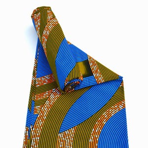 Könnte beinhalten: Gerollter Stoff mit einem lebendigen Muster. Das Design zeigt blaue, olivgrüne, orangefarbene und weiße geschwungene Linien und Streifen. Der Stoff ist gefaltet und gerollt, wodurch das komplizierte Muster zur Geltung kommt.