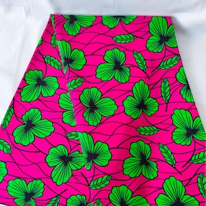 May include: Bright pink fabric with a repeating pattern of green shamrock-like flowers and leaves. The flowers have black centers and are outlined in green. The background features thin, wavy black lines.