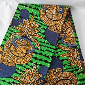 May include: Vibrant green fabric with a repeating pattern of orange and blue stylized floral and geometric shapes. The fabric has a wavy green background with black accents, creating a bold and colorful design. This fabric is suitable for various sewing projects.