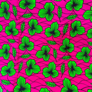 May include: A vibrant fabric featuring a repeating pattern of green shamrock-like leaves and smaller leaves against a bright pink background. The leaves have dark blue-green centers and are outlined in bright green.