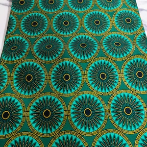 May include: A vibrant green fabric with a repeating circular pattern. Each circle features a black center, surrounded by a teal ring and a gold-colored outer ring. The design is reminiscent of a stylized flower or sunburst.