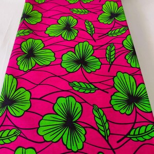 May include: Bright pink fabric with a repeating pattern of large green and black floral designs and green leaves. The fabric has a wavy, textured appearance, creating a visually dynamic textile.