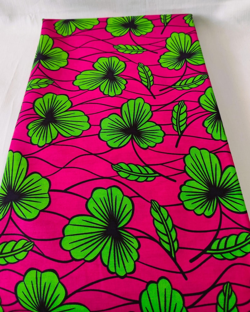 May include: Bright pink fabric with a repeating pattern of large green and black floral designs and green leaves. The fabric has a wavy, textured appearance, creating a visually dynamic textile.