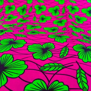 May include: A vibrant fabric with a repeating pattern of green flowers and leaves on a bright pink background. The floral design is outlined in black, creating a bold contrast. The fabric's texture appears soft and flowing.
