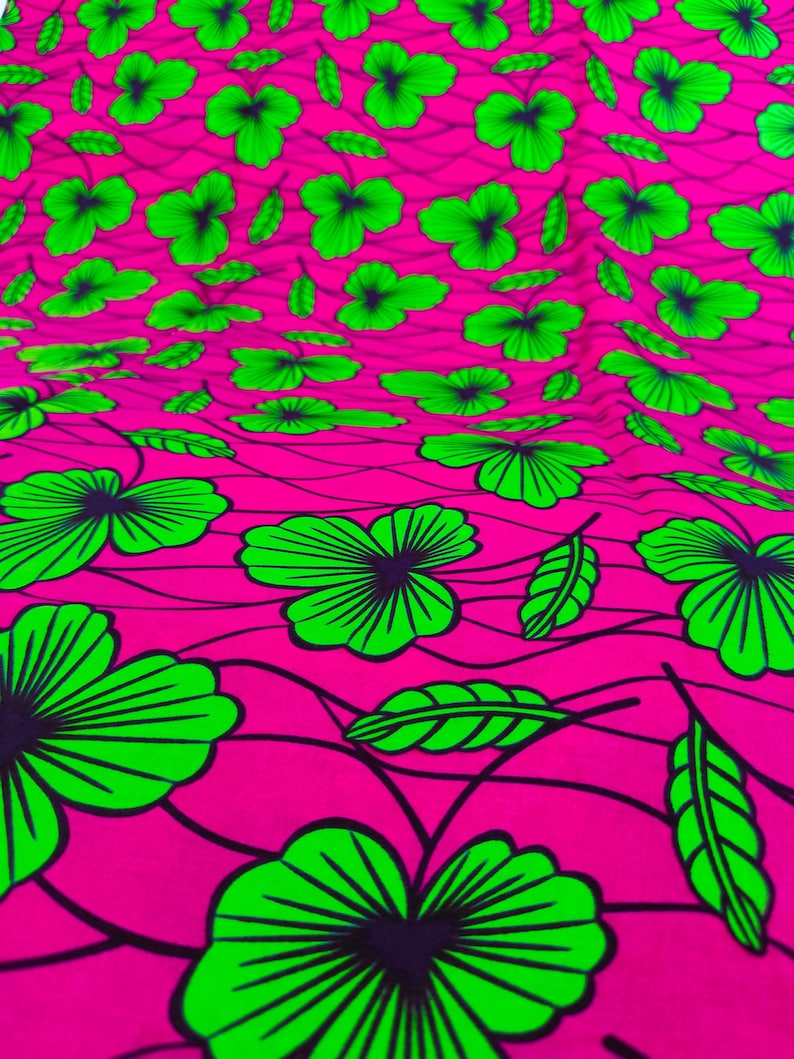 May include: A vibrant fabric with a repeating pattern of green flowers and leaves on a bright pink background. The floral design is outlined in black, creating a bold contrast. The fabric's texture appears soft and flowing.