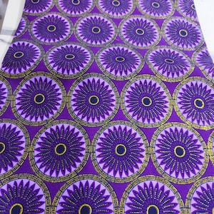 Könnte beinhalten: Ein lebendiger violetter Stoff mit einem sich wiederholenden Blumenmuster. Jede Blume hat eine dunkelviolette Mitte, umgeben von einem goldenen Ring und einem Ring aus violetten Blütenblättern. Der Hintergrund ist einfarbig violett.