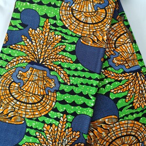 May include: Vibrant green fabric with a repeating pattern of orange and yellow fan-like shapes, blue circular designs, and black wave-like lines. The fabric has a bold, colorful design.