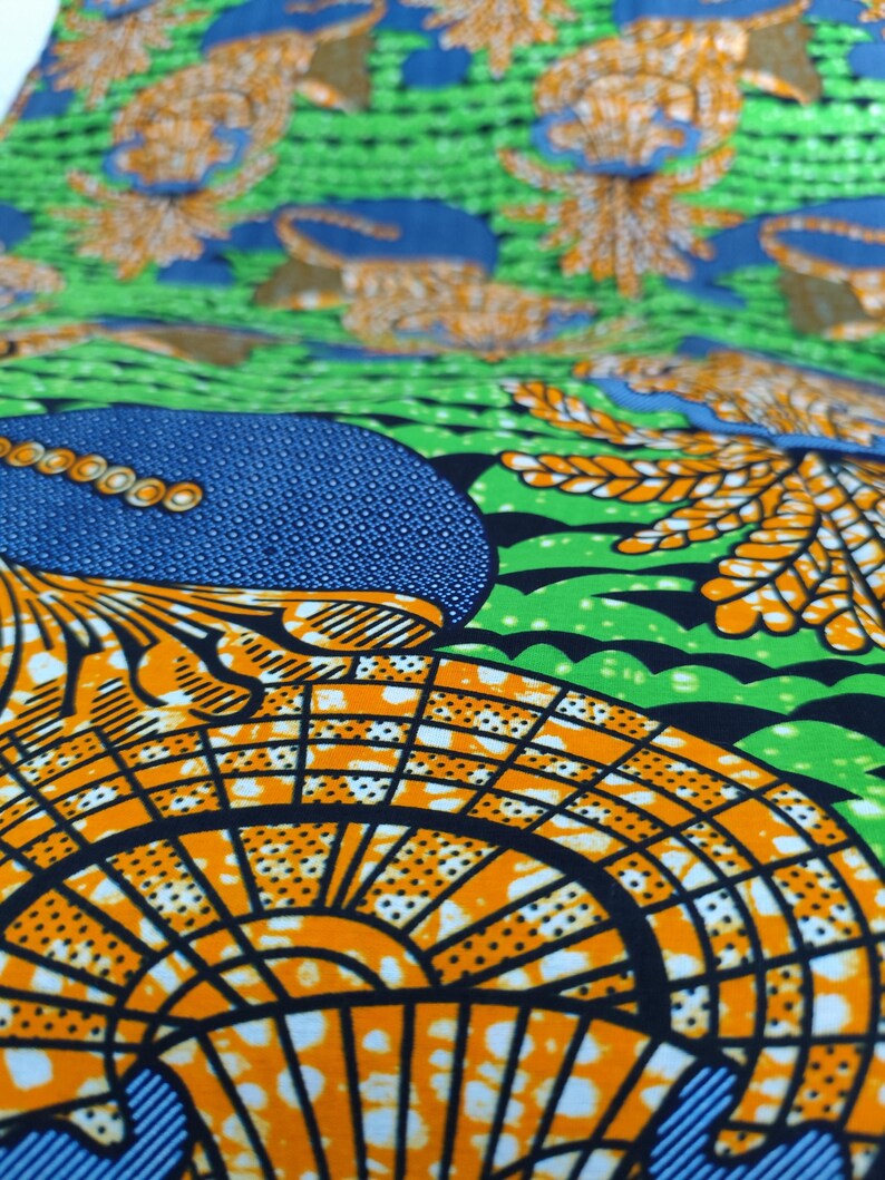 May include: Close-up of a vibrant fabric with a repeating pattern. The design features orange, blue, and green elements. The orange sections have a grid-like pattern with small white dots. The blue sections have a dotted texture. The green sections have a wavy design.