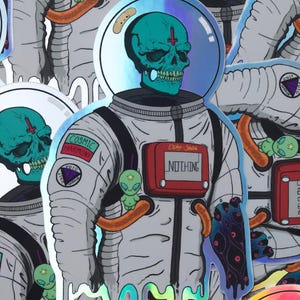 May include: Holographic sticker featuring an astronaut with a teal skull head and a red cross. The astronaut suit has the text "NOTHING" and "COSMIC HARMONY". A small green alien is also present. The sticker has a unique, dripping effect.