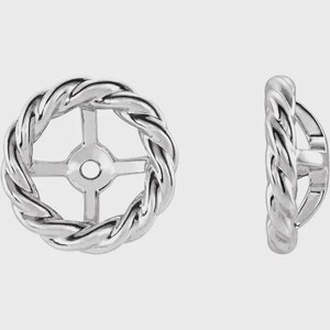 May include: Two silver earring jackets with a twisted rope design. One earring jacket is shown from the front, and the other is shown from the side. The jackets have a circular design with a cross-shaped support in the centre.
