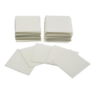 May include: A stack of white, square, absorbent cloths. There are two stacks of cloths, each with about 20 cloths, and several individual cloths laid out on a white surface.