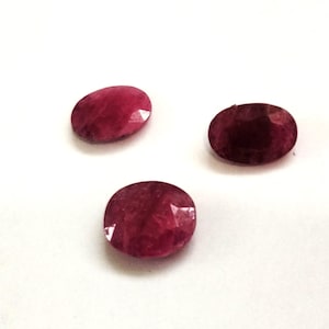 May include: Three oval-shaped, faceted gemstones in varying shades of red. The gems are displayed against a white background, showcasing their polished surfaces and internal clarity. These gemstones are suitable for jewelry making.
