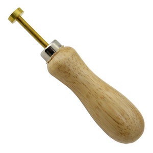 May include: A brass and wood tool with a round head and a wooden handle. The tool is used for punching holes in leather.