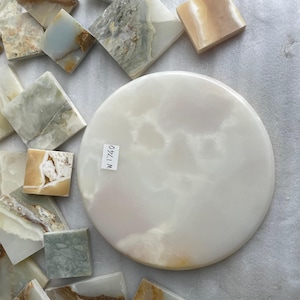 May include: An assortment of natural stone tiles in different shapes and colours. A large, round, white stone piece is visible, with a label reading "W 1740". Square and diamond-shaped tiles in white, beige, and green surround the round piece, creating a varied display.