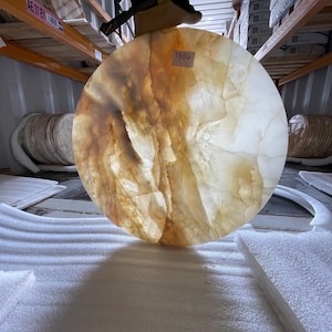 May include: A large, circular, translucent stone slab in shades of amber and cream. The stone features a natural, veined design and is being held up. The slab is labelled with the number "1554".