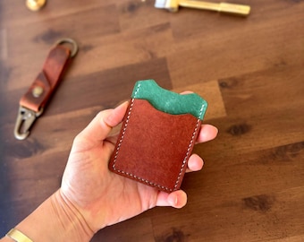 May include: A brown leather card holder with a green leather interior. The card holder is being held in a hand.