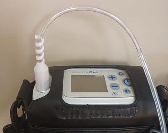 May include: A portable oxygen concentrator with a black carrying case and a clear oxygen tube. The device has a digital display with the text "INOGEN ONE" and buttons for control.