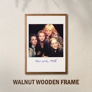 May include: A framed photograph featuring four women, with the handwritten text "New York, 1998" at the bottom. The frame is made of walnut wood. The image is mounted on a white background.