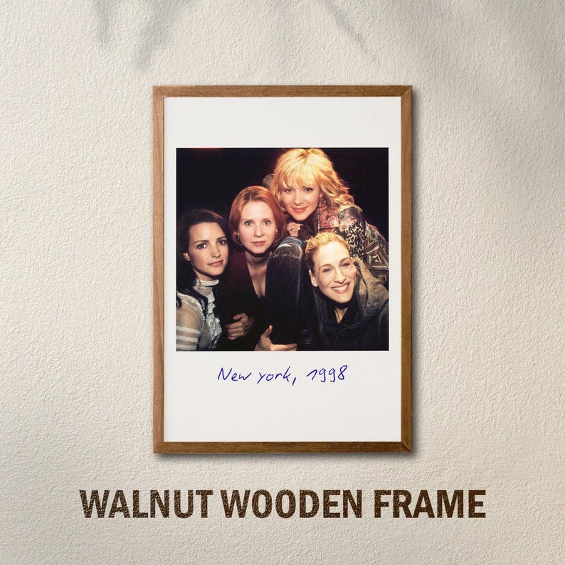 May include: A framed photograph featuring four women, with the handwritten text "New York, 1998" at the bottom. The frame is made of walnut wood. The image is mounted on a white background.