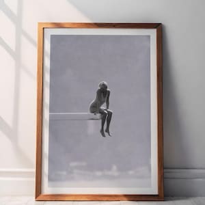 May include: Monochrome framed art print featuring a person seated on a diving board. The artwork is presented in a wooden frame and is set against a white wall. The image has a minimalist aesthetic.