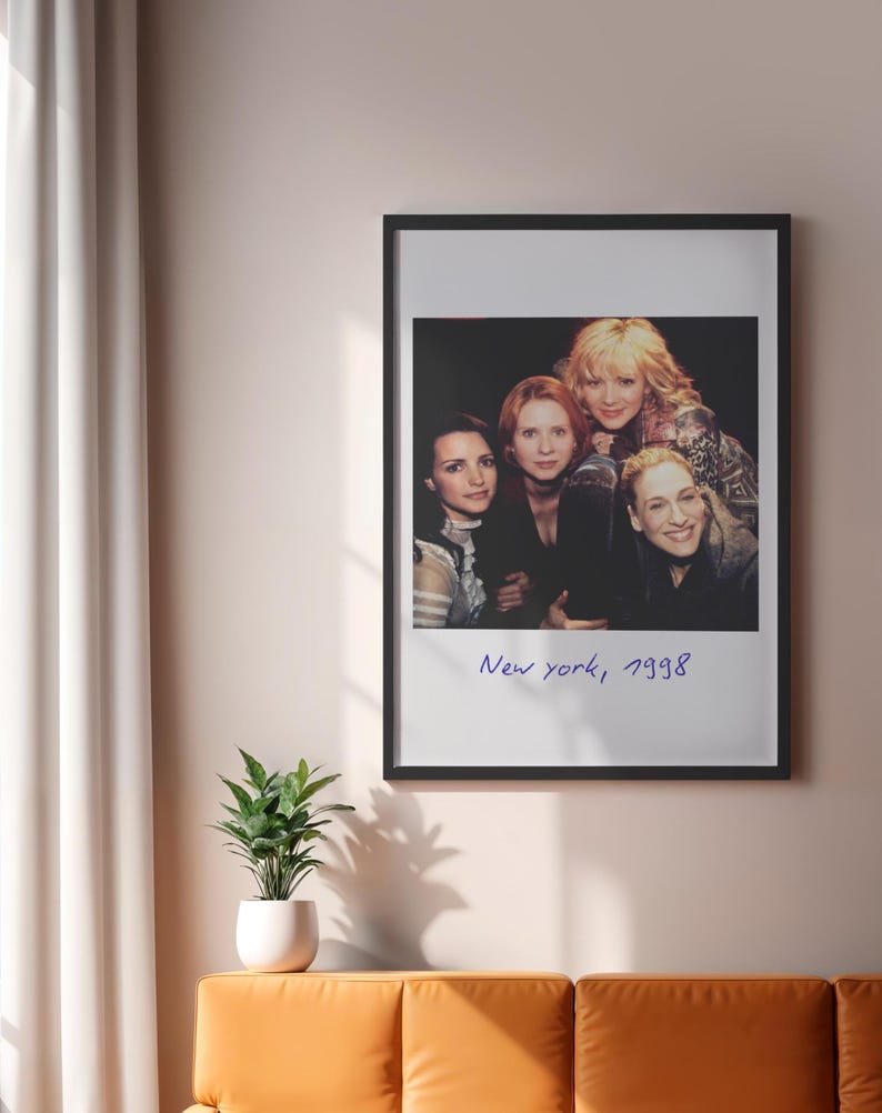 May include: A framed print featuring a group of four women. The image is in a black frame and has the text "New york, 1998" in a handwritten style. The print is hanging on a light pink wall.