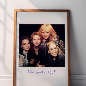 May include: A framed print featuring a group of four women posing for a photo. The image is a vintage-style Polaroid with the handwritten text "New york, 1998" in blue ink. The frame is made of wood.
