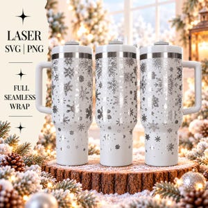 May include: Three white tumblers with handles, each featuring a silver snowflake pattern wrap. The tumblers have a metallic rim and a lid. Text on the left side reads: LASER SVG | PNG FULL SEAMLESS WRAP. The design displays various snowflake shapes.