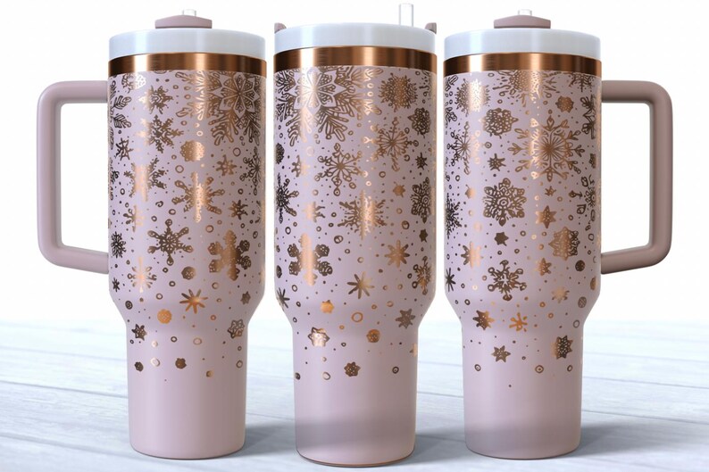 May include: Three insulated tumblers with a light pink base and a white lid. The tumblers feature a gold snowflake pattern and a matching handle. The rim is accented with a gold band. The tumblers are approximately 25 cm tall.
