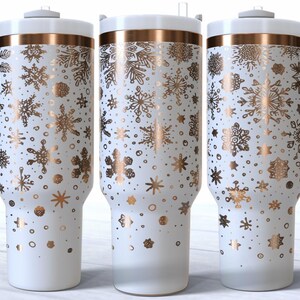 May include: White insulated tumbler with a gold snowflake pattern. The tumbler has a white handle and lid with a gold band. The design features various snowflake shapes and dots. The tumbler is designed to hold approximately 887 ml.