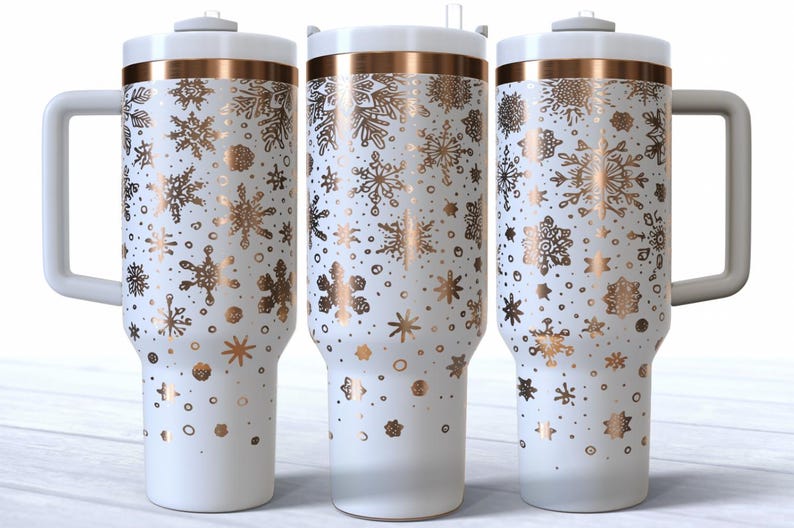 May include: White insulated tumbler with a gold snowflake pattern. The tumbler has a white handle and lid with a gold band. The design features various snowflake shapes and dots. The tumbler is designed to hold approximately 887 ml.