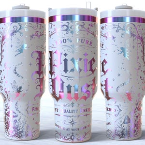 May include: A white stainless steel tumbler with a handle and a straw, featuring an iridescent, holographic fairy-themed design. The text reads 100% PURE PIXIE DUST, FINEST QUALITY UNFILTERED, and GENUINE AT YOUR OWN RISK, surrounded by floral and fairy motifs.