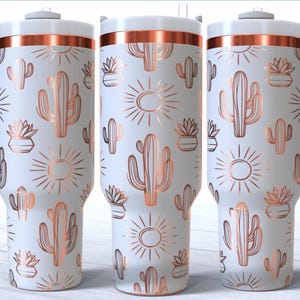 May include: White travel mug with a copper-colored band and handle. The mug is decorated with a repeating pattern of cacti, potted succulents, and sunbursts in a copper color. The mug has a white lid.