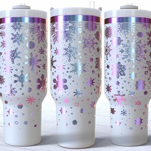 May include: Three white insulated tumblers with a handle, decorated with iridescent snowflakes in shades of pink, purple, and blue. The tumblers have a white lid and a silver band around the top. The design is a winter theme.