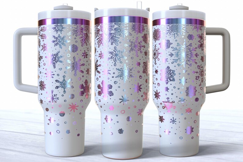 May include: Three white insulated tumblers with a handle, decorated with iridescent snowflakes in shades of pink, purple, and blue. The tumblers have a white lid and a silver band around the top. The design is a winter theme.
