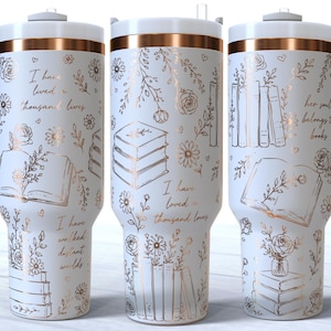 Puede incluir: Un vaso de acero inoxidable blanco con asa, que presenta dibujos de líneas en oro rosa de libros y flores, junto con los textos "I have lived a thousand lives," "I have walked distant worlds," y "her soul belongs to books" en la superficie.