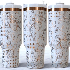 Könnte beinhalten: Drei weiße Becher mit kupferfarbenen Erdbeer- und Rankenmustern. Jeder Becher verfügt über einen weißen Deckel, einen kupferfarbenen Rand und einen weißen Henkel an der Seite. Das Design zeigt detaillierte Illustrationen von Erdbeeren, Blättern und Ranken.