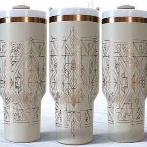 May include: Three insulated travel mugs with a cream-colored body, white lid, and a gold-colored band. The mugs feature a geometric design in gold and black. Each mug has a light gray handle.